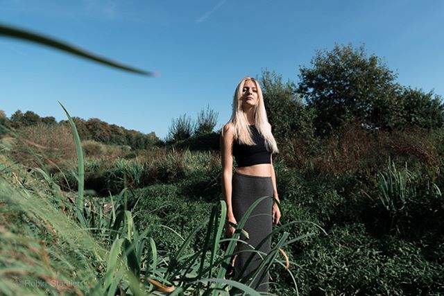 A blonde woman in sportswear stands in a field on a sunny day.