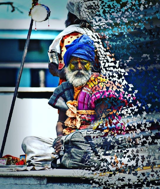 A sadhu with a blue turban sits in meditation, his face marked with yellow paint, creating a moment of serene intensity.