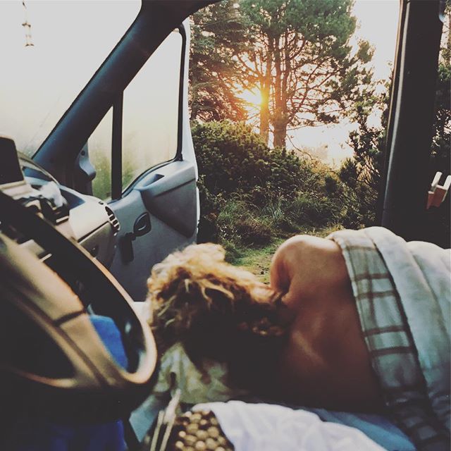 Person relaxing in a van, enjoying the view of nature and the rising sun.