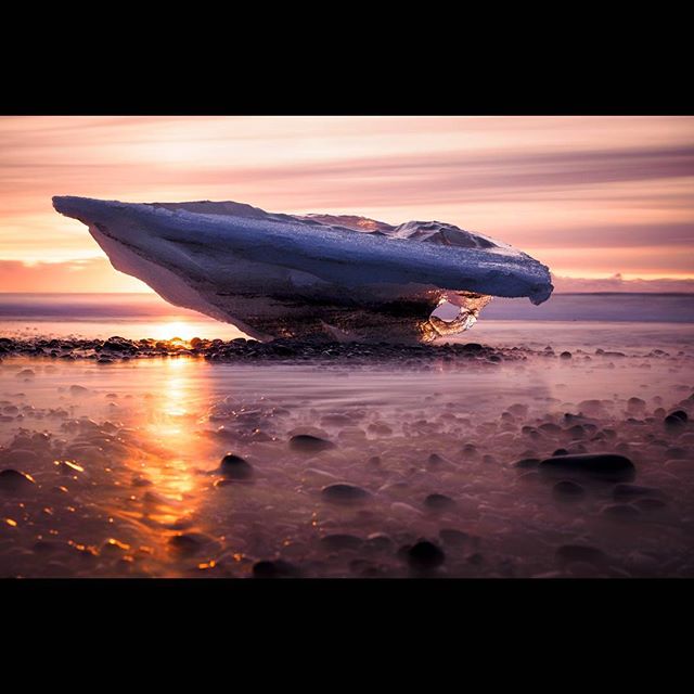 A mesmerizing sunset illuminates an icy landscape on a rocky beach, creating a tranquil and scenic coastal view.