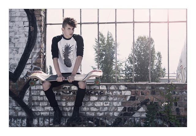 A young man sits with his skateboard against a brick wall in an urban setting.