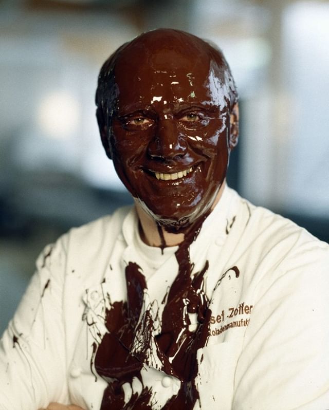 A smiling chef is covered in chocolate, showcasing his love and dedication to the art of chocolate making.