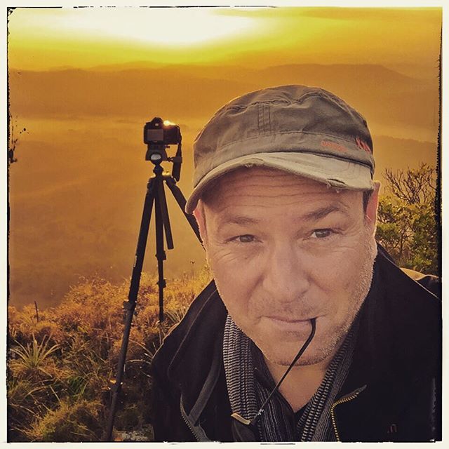 A man with a camera and tripod enjoys a sunrise on a mountain.