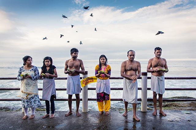 A family stands together during a beachside ceremony with birds flying overhead, captured in a cultural moment.