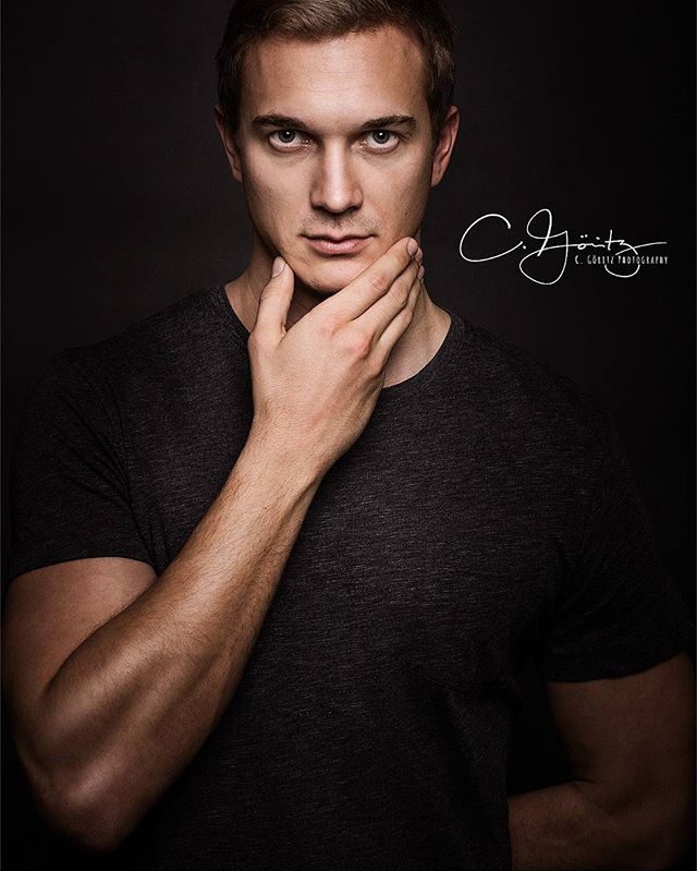 A man poses in a studio portrait, thoughtfully touching his chin against a dark backdrop.