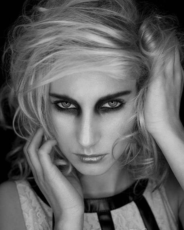 A monochrome headshot of a blonde woman with dark makeup in an editorial fashion style.