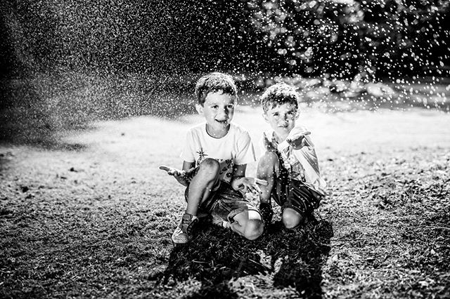 Two boys play in the sprinklers on a sunny day, enjoying childhood fun in black and white.