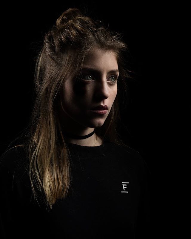 A striking portrait of a young woman in a dark setting, showcasing a minimalist and moody aesthetic.