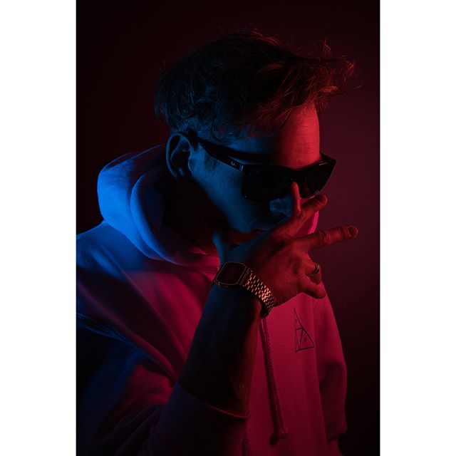 Stylish man wearing sunglasses and a hoodie in a studio with creative lighting.