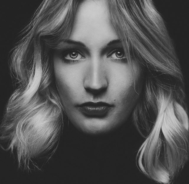 A black and white studio portrait of a woman with blonde wavy hair and dark lipstick.