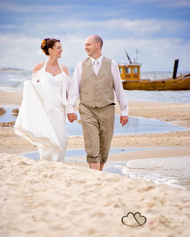 A bride and groom walk hand-in-hand along a beach on their wedding day.
