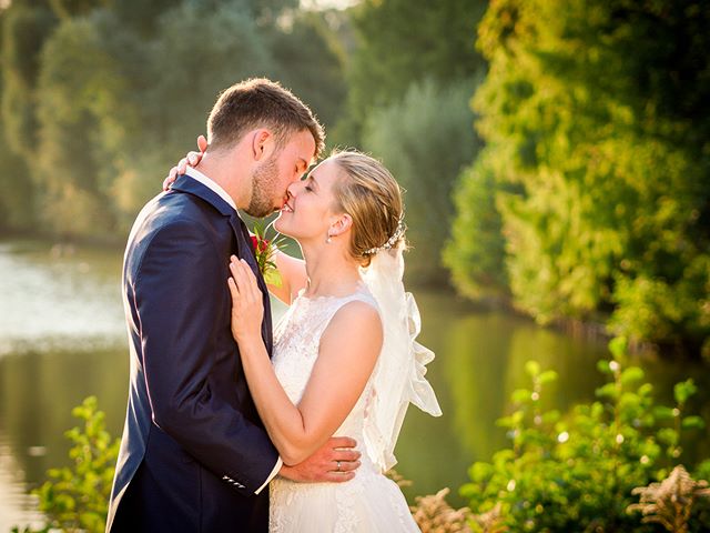 A bride and groom share a kiss by a tranquil lake on their wedding day.