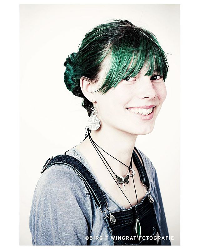 A cheerful woman with green hair smiles in a bright studio portrait.