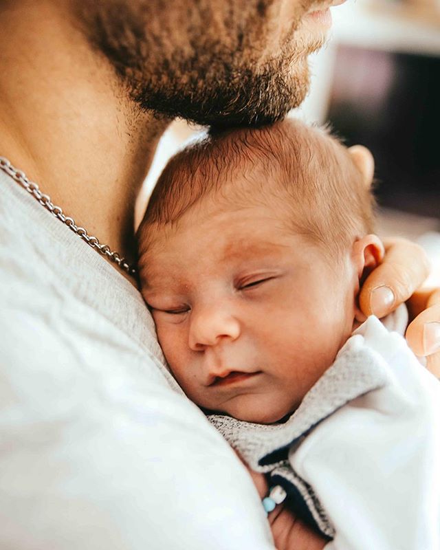 A father holds his newborn baby in a close, intimate embrace, conveying love and tenderness.