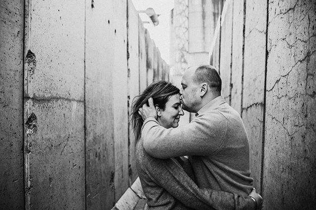 A couple embraces in an urban alleyway, sharing a tender moment in black and white.