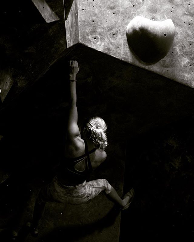 A strong woman rock climbs in a gym, showcasing fitness and determination in a monochrome aesthetic.