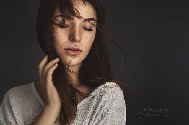 Portrait of a serene woman with freckles, eyes closed, in a soft, intimate setting.
