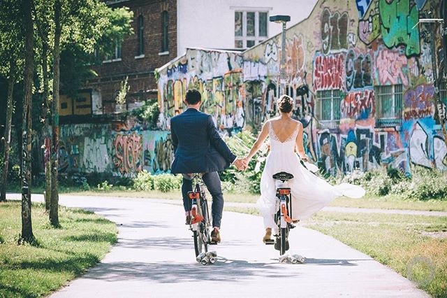 A bride and groom ride bikes hand-in-hand, their love story unfolds against a backdrop of vibrant street art.