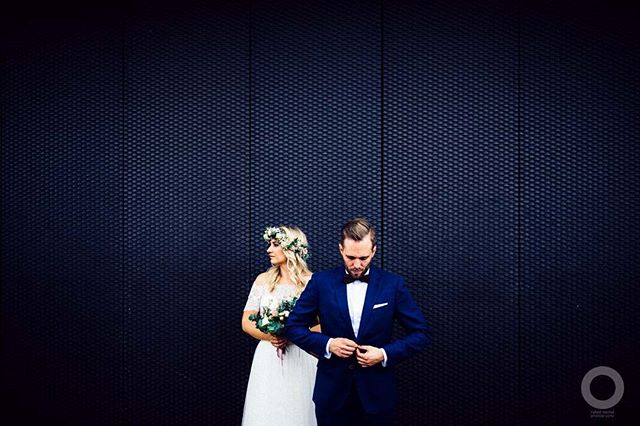 A bride and groom pose against a dark blue textured wall on their wedding day.