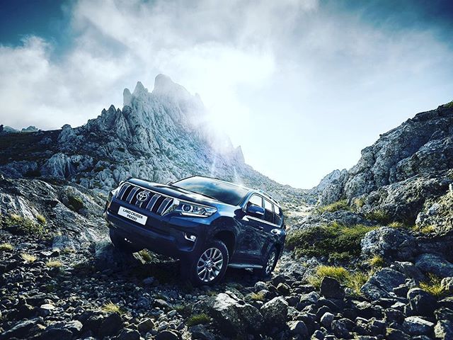 A blue Land Cruiser Prado conquers rocky mountain terrain, showcasing adventure and automotive power.