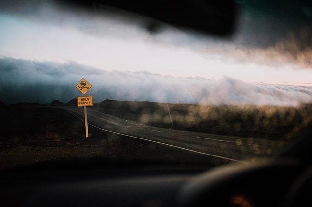 A winding road through a misty landscape is seen from inside a car with a road sign warning of icy conditions.