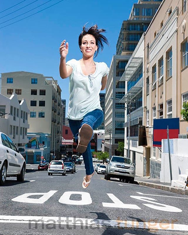 A cheerful woman energetically runs across a city street on a sunny day.