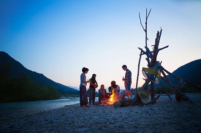 Group of friends gathering around a campfire next to a river.