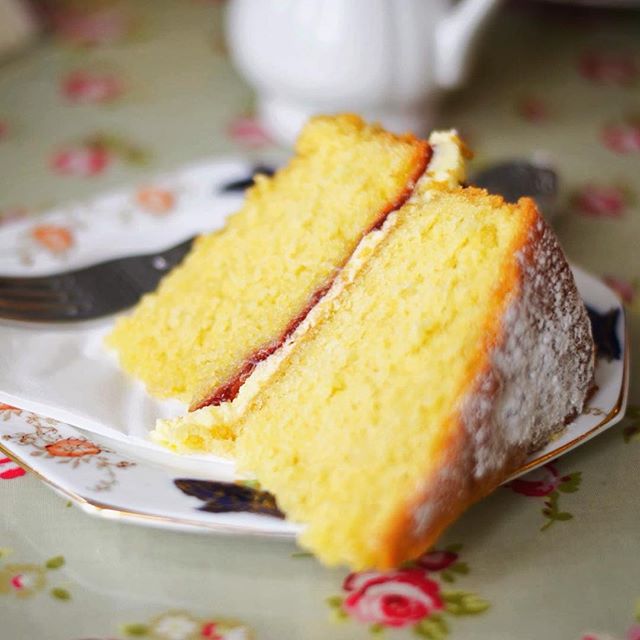 Two slices of cake with jam and cream filling sit on a floral patterned plate on a matching tablecloth.