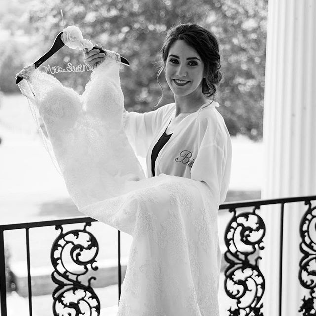 A bride smiles while holding her wedding dress on the hanger on the balcony.
