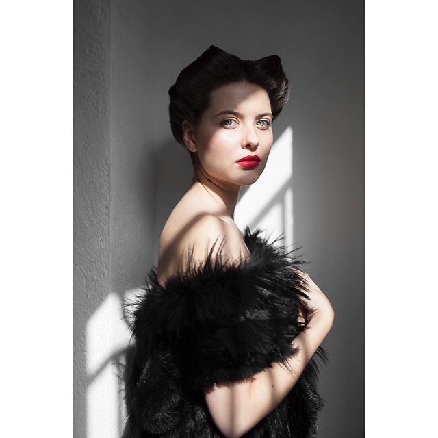 Elegant woman with red lipstick and fur stole poses in soft light.