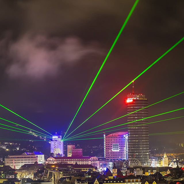 City skyline illuminated by green laser beams at night, creating a vibrant and modern cityscape.