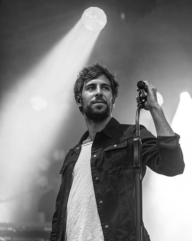 A singer performs with a microphone on stage, illuminated by bright lights in a black and white image.