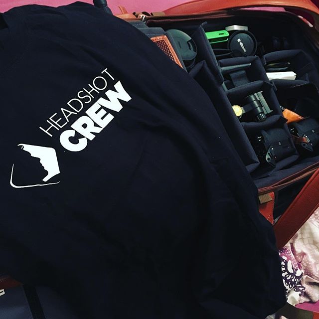 A black "Headshot Crew" t-shirt laid beside an open camera bag.