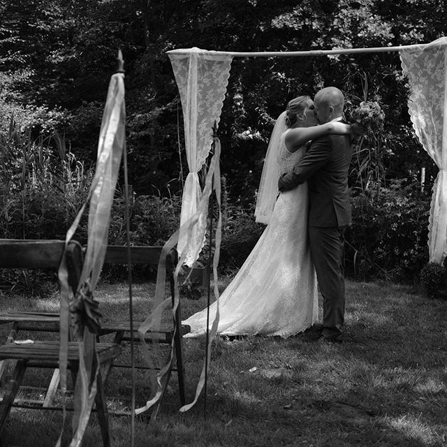 A bride and groom share a kiss during their black and white wedding ceremony in a lush garden setting.