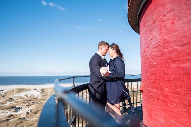 A couple embraces on a lighthouse balcony overlooking the sea in a romantic moment.