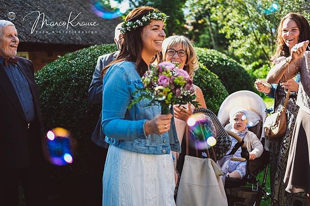 A happy bride celebrates her wedding with guests in a sunlit garden with a baby in a stroller.
