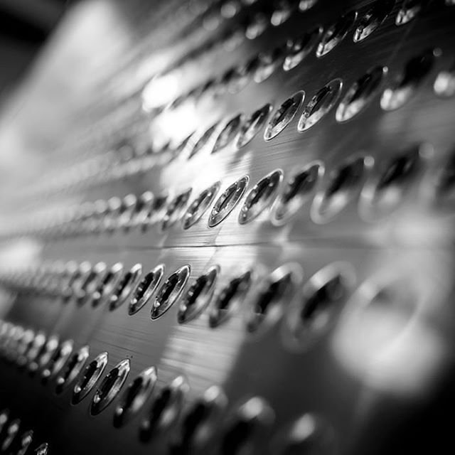 A close-up, abstract view of a metal surface with rows of rivets creates a strong industrial texture and visual pattern.