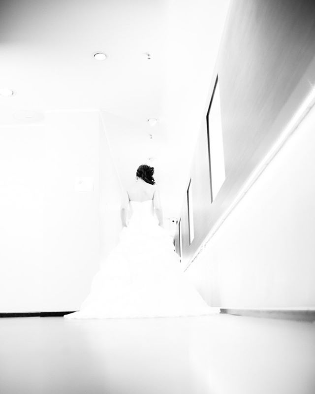 A bride in a white wedding dress walks down a hallway, captured in a black and white photograph.