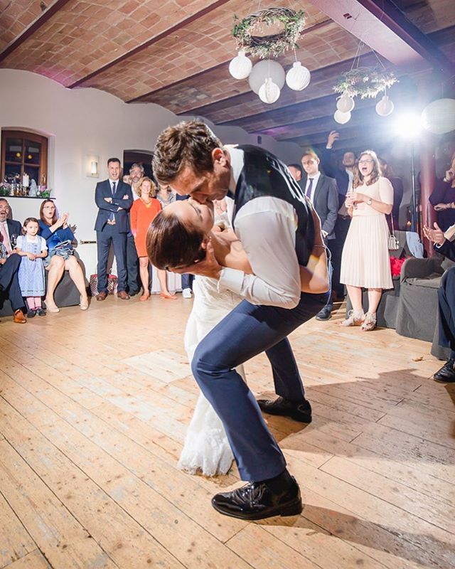 A bride and groom share a kiss on the dance floor at their wedding reception as guests look on.
