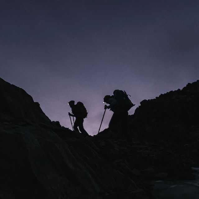 Silhouetted hikers with headlamps ascend a dark mountain path at night, showcasing adventure and determination.