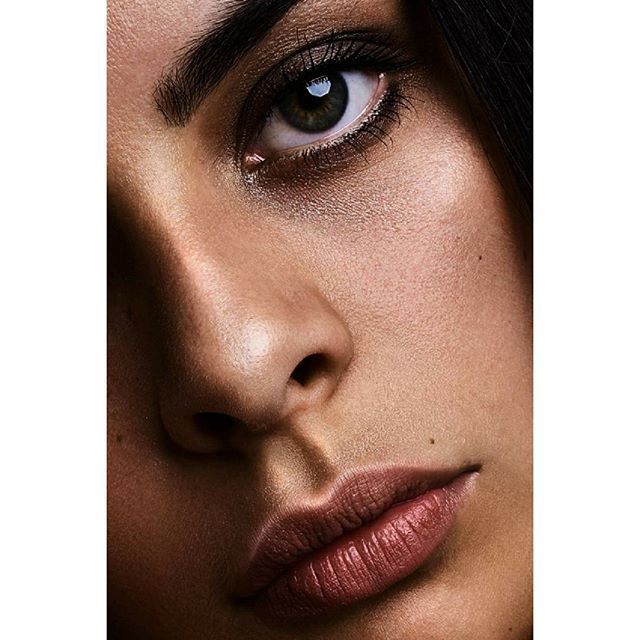 A striking close-up showcases a woman's eye, lips, and flawless skin in a beauty editorial.