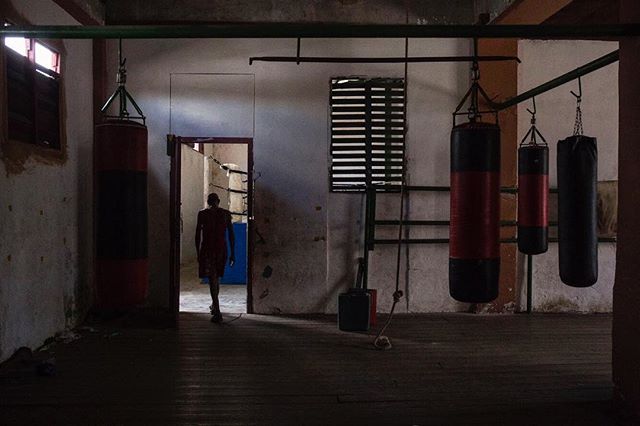A man walks through a dimly lit boxing gym with punching bags.
