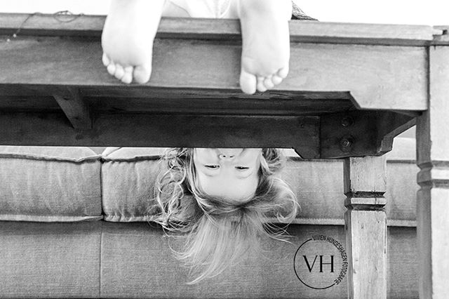 A child's feet are seen above a table, with the child playfully looking down, shot in black and white.