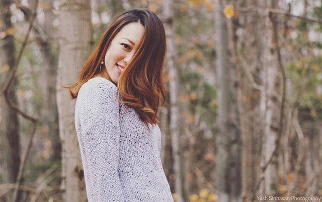 Smiling woman with brown hair poses in front of a wooded background in autumn.