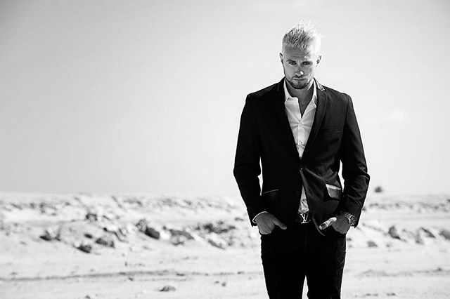 A stylish man in a suit stands in a stark landscape, projecting confidence and sophistication in monochrome.