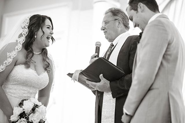 A bride laughs during her wedding ceremony, alongside her groom and the officiant.