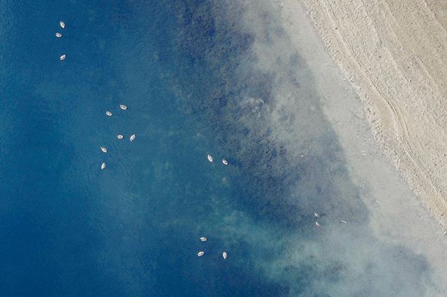 Aerial view of small boats sailing in calm, blue water near a sandy beach, creating a serene coastal scene.