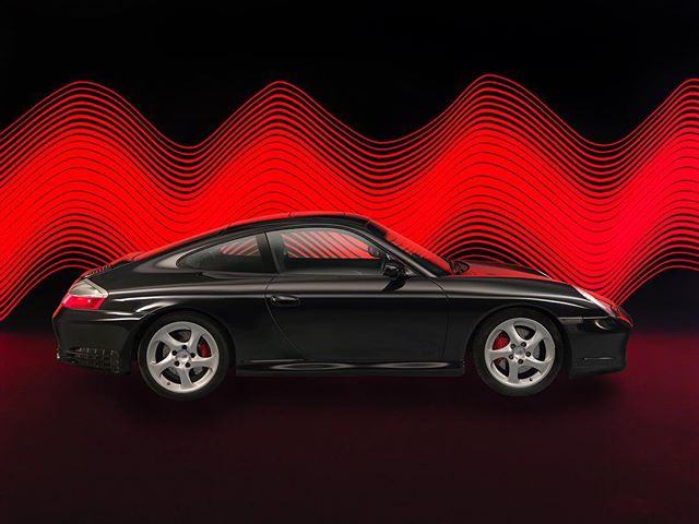 A black Porsche coupe stands out against a red-lined background in a studio setting, ideal for automotive campaigns.
