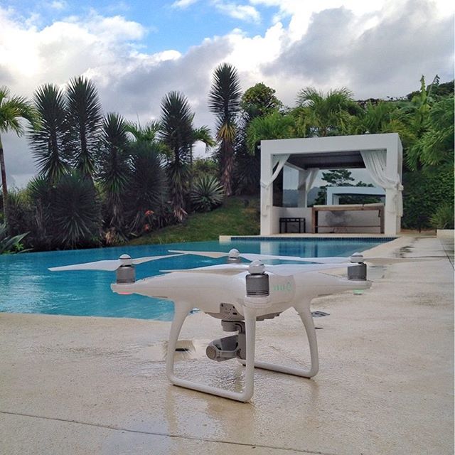 A white drone sits on a patio next to a blue swimming pool with a white gazebo in the background.