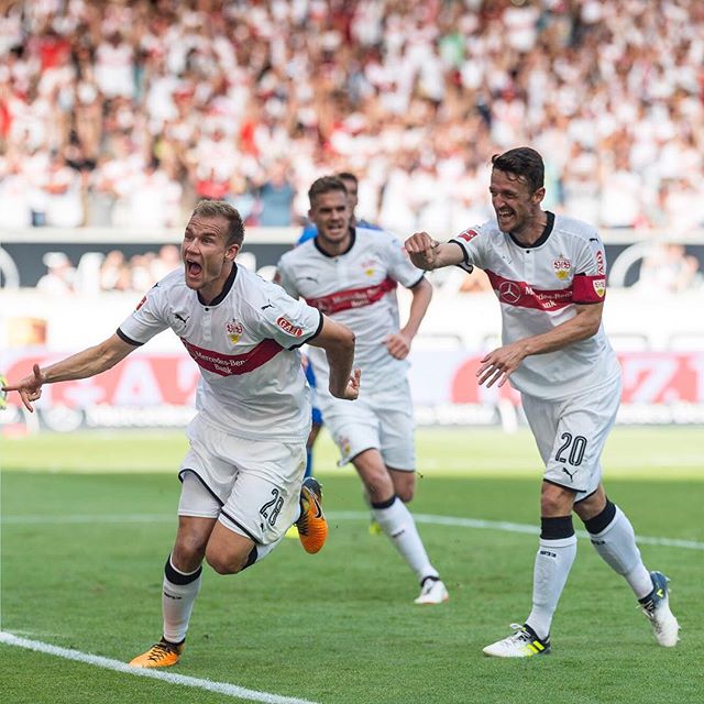 Soccer players celebrate on the field in a stadium filled with fans during a sunny day.